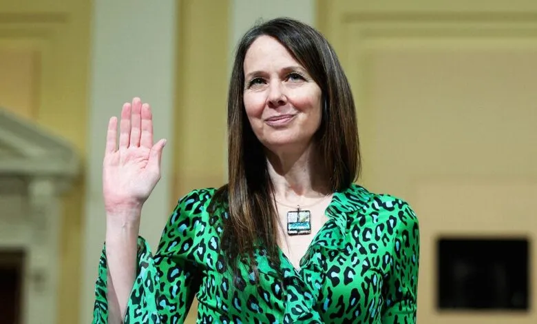 Jen Easterly raises her hand, wearing a green patterned blouse.