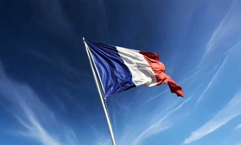 French flag waving against a bright blue sky with wispy clouds.