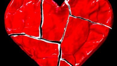 Cracked red heart on black background, symbolizing heartbreak and emotional pain.