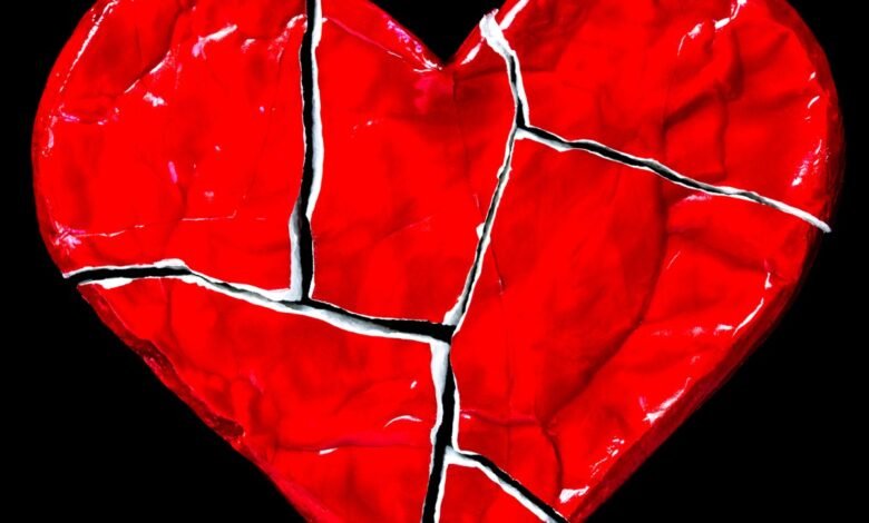 Cracked red heart on black background, symbolizing heartbreak and emotional pain.