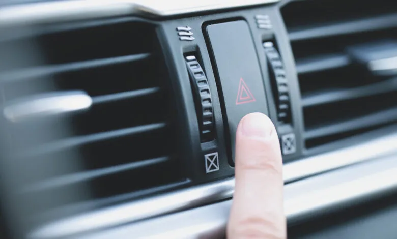 Finger presses hazard light button on car dashboard.