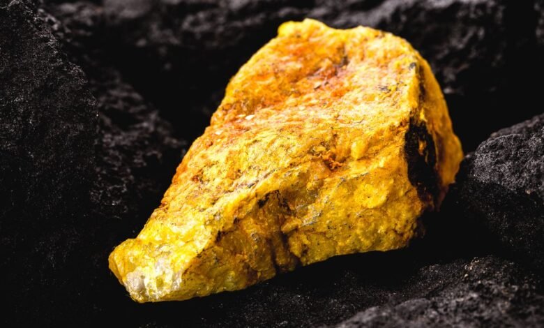 Chunk of yellow rock sits on a bed of dark, volcanic rock.