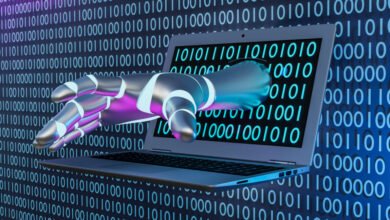 Metallic robot hand extends from laptop screen with binary code background.