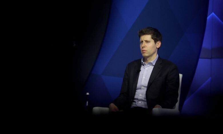 Man in suit sits against blue geometric backdrop, looking serious.