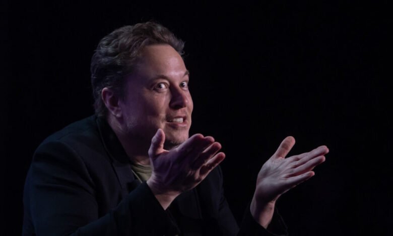 Elon Musk speaks with expressive hand gestures against dark backdrop.