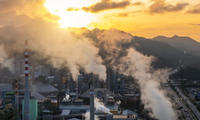 Industrial factory emits smoke against a golden sunset sky.