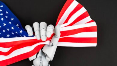 Robot hand holds American flag against a black background.