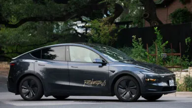 Dark gray Tesla robotaxi driving on a city street.