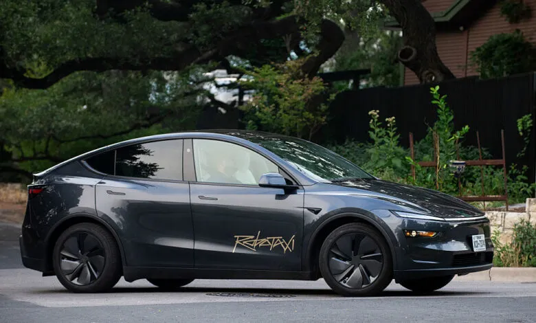 Dark gray Tesla robotaxi driving on a city street.