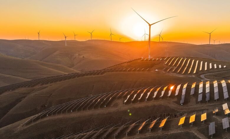 Wind turbines and solar panels on rolling hills at sunset.