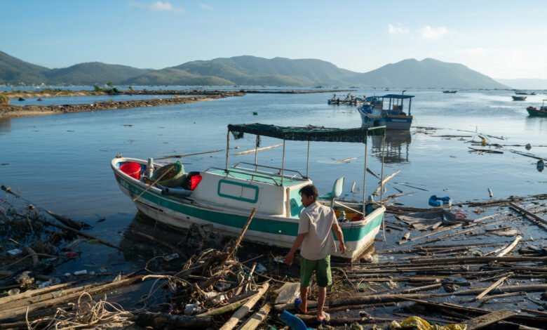 Man stands near boat amidst debris after storm in Vietnam.