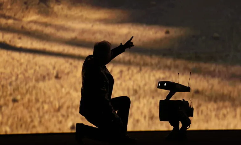 Silhouette of man kneeling next to robot, pointing upwards.