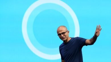 Satya Nadella waves in front of a blue background with a white circle.