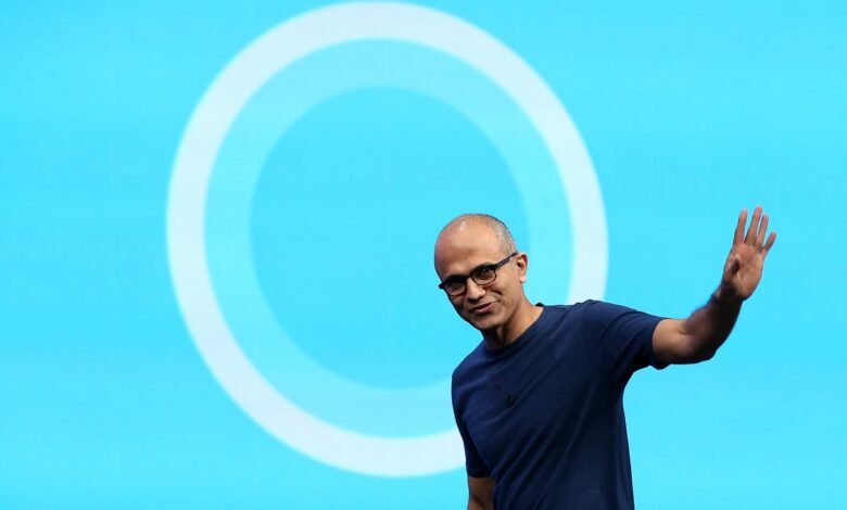 Satya Nadella waves in front of a blue background with a white circle.
