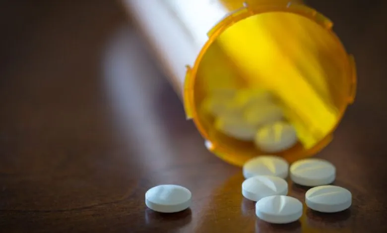 Pills spill from an open orange prescription bottle onto a wood surface.