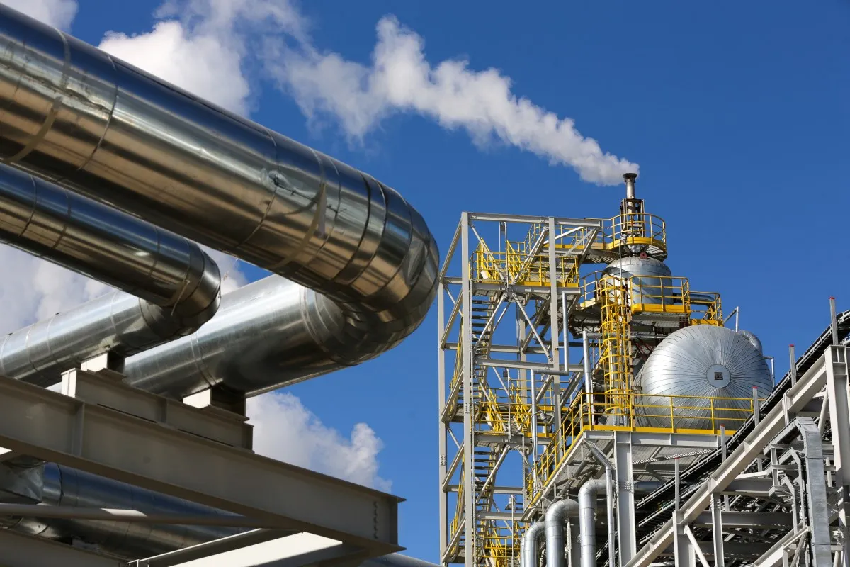 Industrial plant with silver pipes and white smoke against a blue sky.
