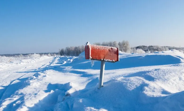 Red mailbox covered in frost stands in a snow-covered landscape under a clear blue sky.
