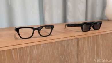 Two pairs of black smart glasses on a light wood surface.