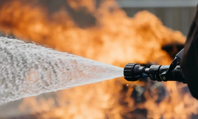 Water stream from nozzle aimed at flames, fire safety demonstration.