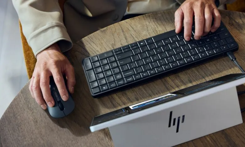 Hands using HP keyboard, mouse, and tablet on a wooden table.