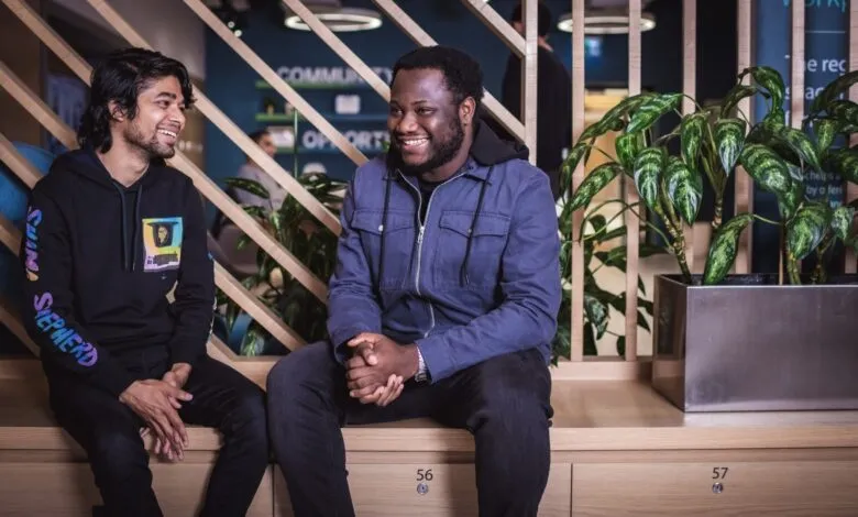 Two young men smiling and talking while sitting in a modern office space.