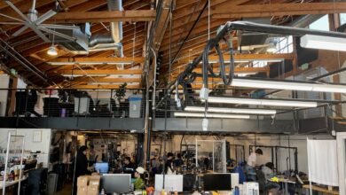 Busy open office space with exposed wooden beams and multiple workstations.