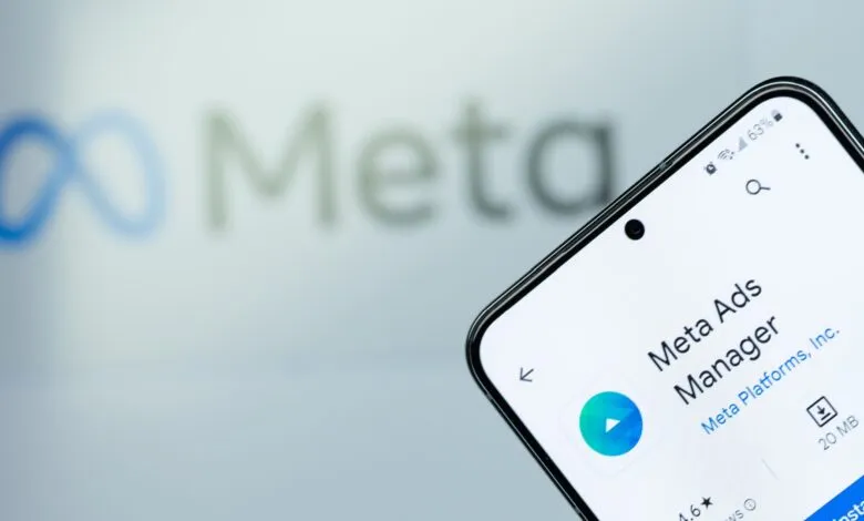 Phone displaying Meta Ads Manager app against blurred Meta logo background.