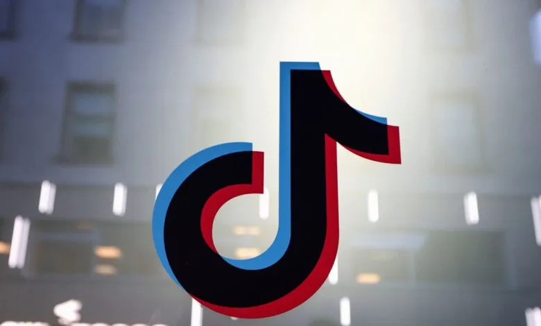 TikTok logo with red and blue offset against a blurred building background.