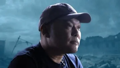 Man in cap with destroyed city backdrop, looking thoughtful.