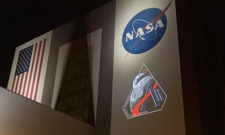 NASA building illuminated with US flag, NASA logo, and Artemis mission patch.