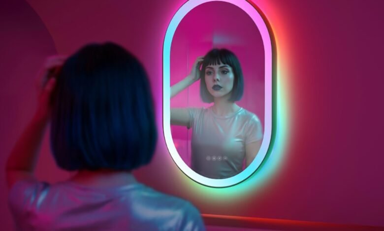 Woman adjusting hair in a vibrant, color-changing LED mirror in a pink room.