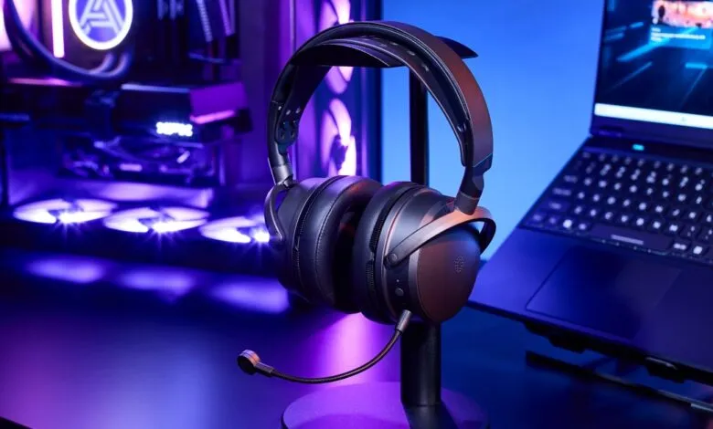 Black gaming headset on stand with PC and laptop in background.