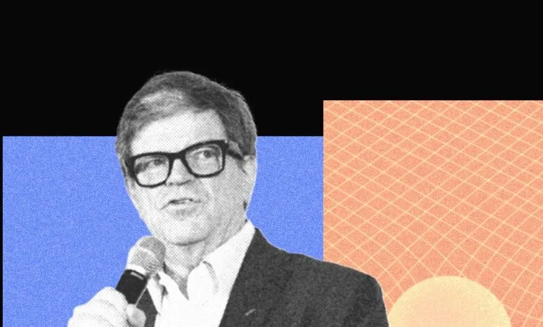 Man with glasses speaks into microphone against geometric background.