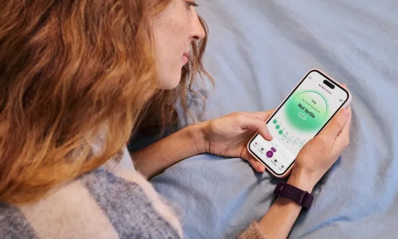 Woman using fertility tracking app on her smartphone in bed.