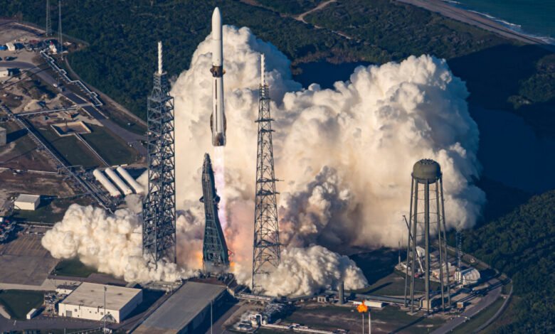 Rocket ascends amidst smoke and support towers, near coastline.