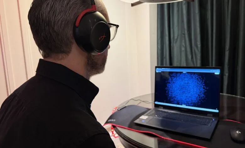 Man wearing HyperX gaming headset looking at laptop screen.