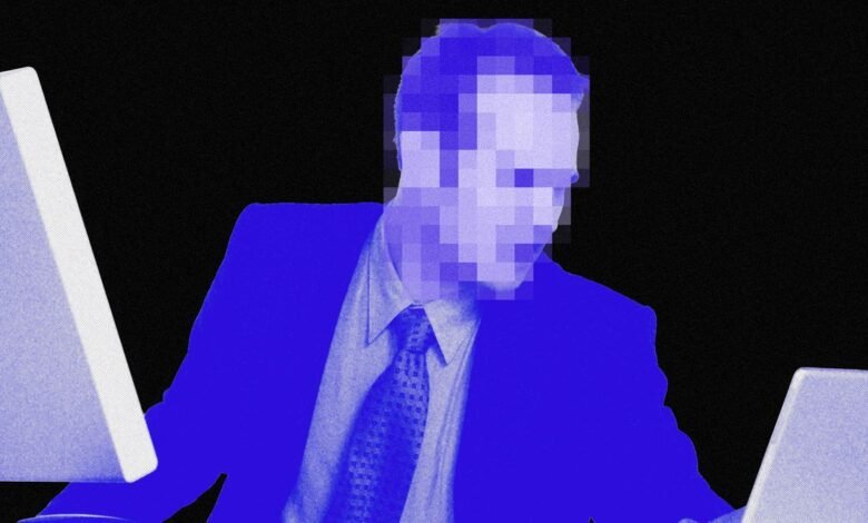 Person in suit works at dual monitors, face pixelated.