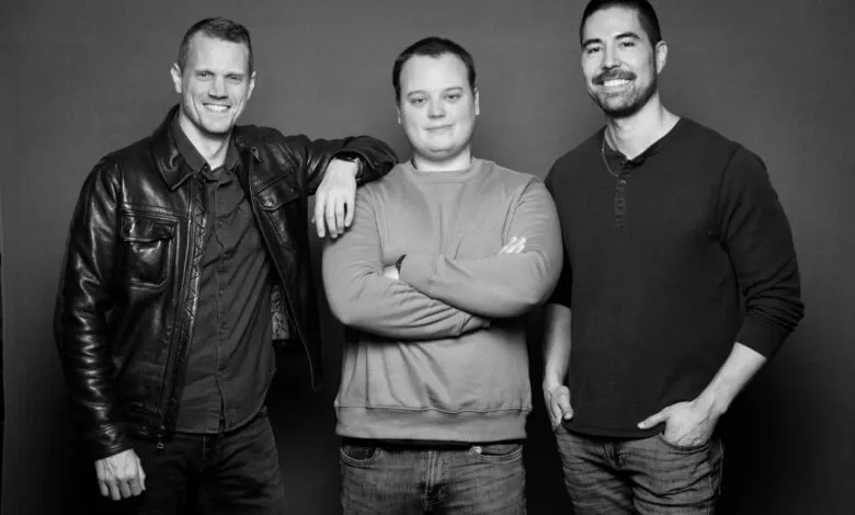 Three men pose together in a black and white studio shot.