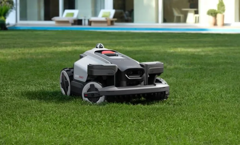 Robotic lawn mower on green grass in front of modern house.