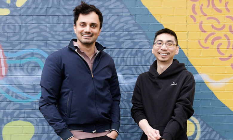 Two men, Zhen Lu and Pardeep Singh, stand smiling in front of a colorful mural.
