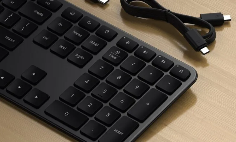 Close-up of a sleek black Satechi keyboard with a USB-C cable on a wooden surface.