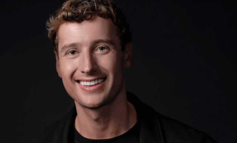 Smiling man with curly hair against a dark background.
