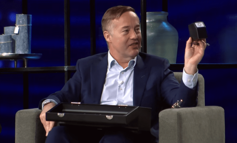 Man in suit holds small black cube on stage.