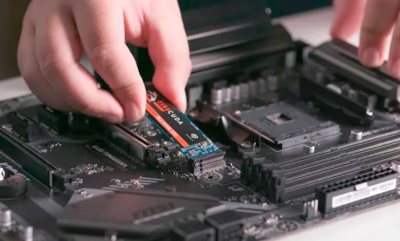 Hands installing a Seagate Firecuda NVMe SSD into a motherboard.