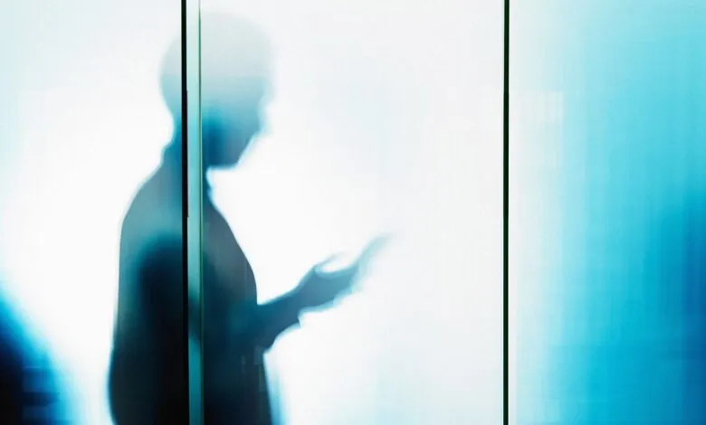 Blurred silhouette of person using phone behind frosted glass.