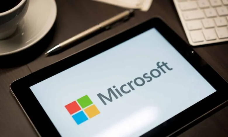 Tablet displaying the Microsoft logo on a desk with coffee and keyboard.