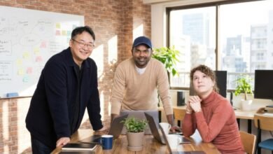 Three smiling founders, Mynseok Kang, Lax Poojary, and Lucie Marchand, pose at a wooden table.