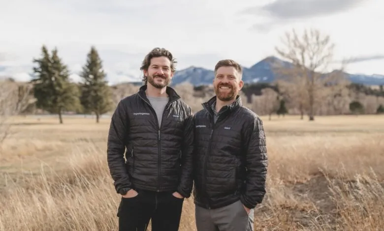 Two men stand outdoors wearing Superorganism jackets, smiling at the camera.