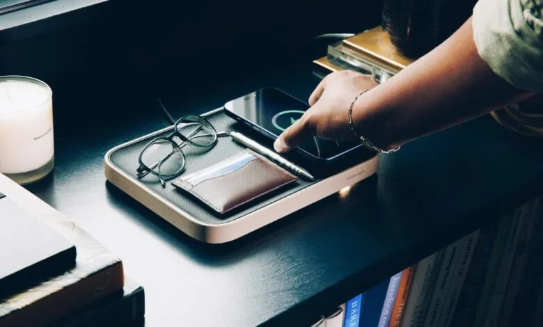 Person placing phone on wireless charging valet tray with accessories.