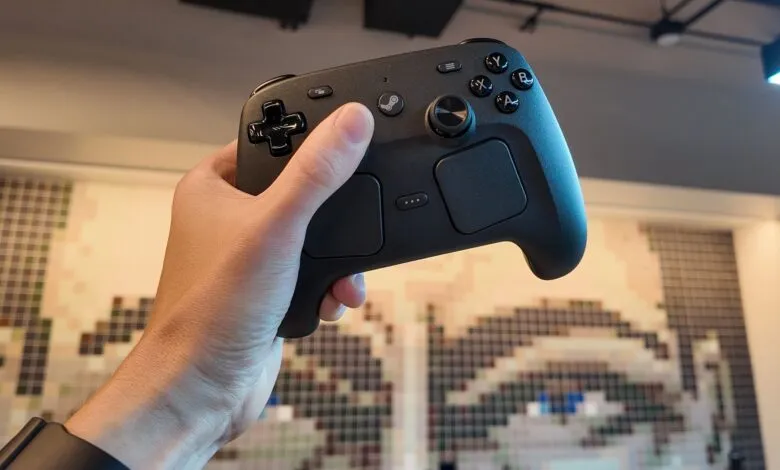 Hand holding a black Steam Controller against pixelated wall art.
